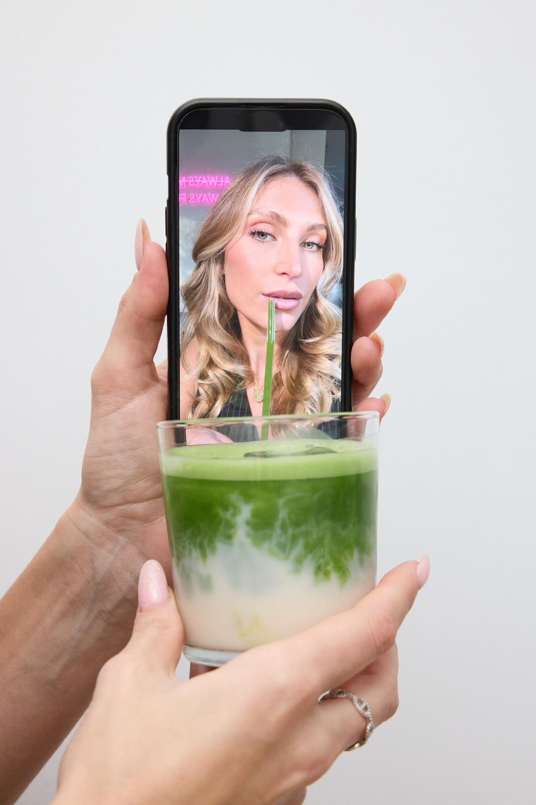 Hand holding a matcha drink with a phone